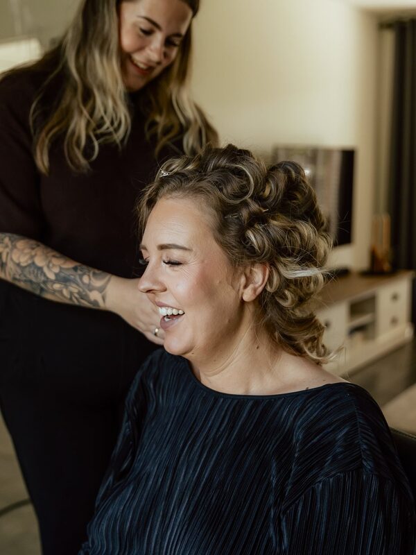 Bruid lacht met krulspelden in haar haar terwijl Danique aan het werk is