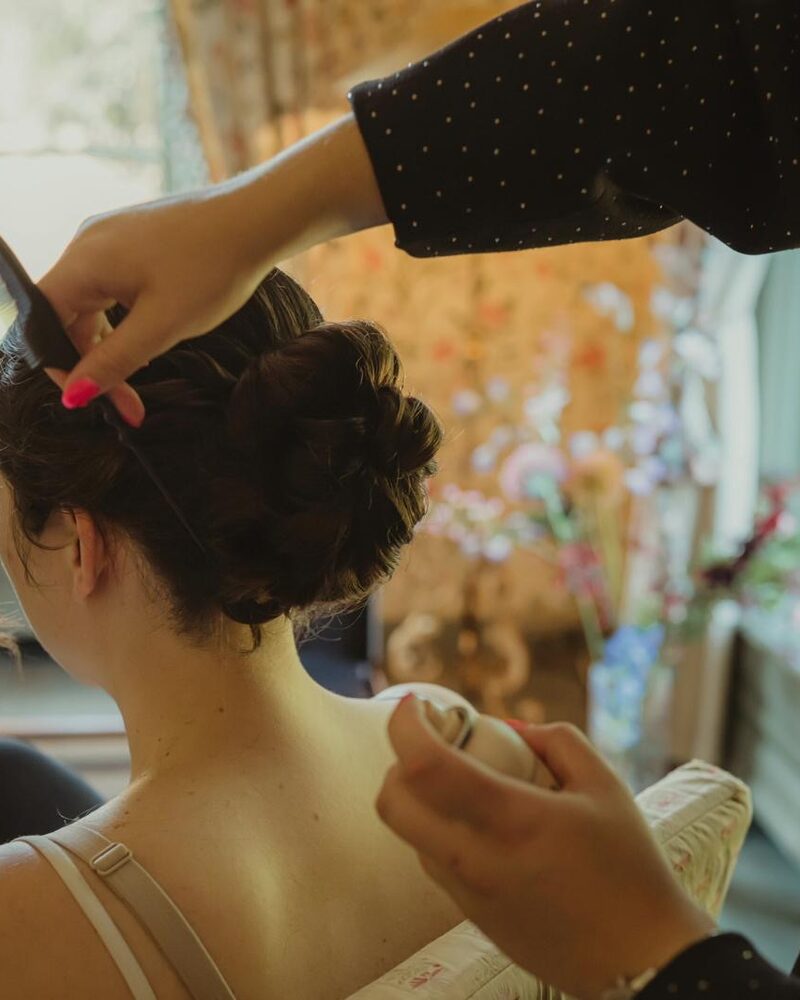 Hand van Danique zet een haarspeld met bloemen vast in een opgestoken bruidskapsel