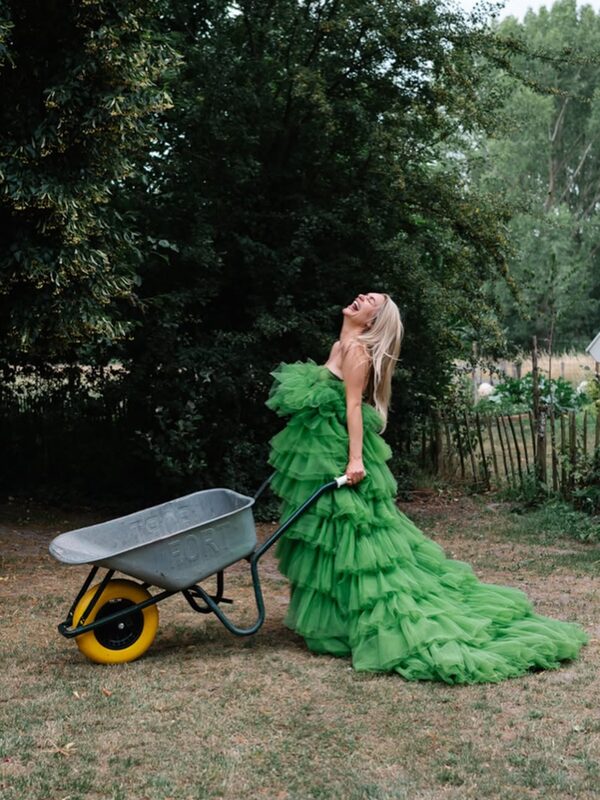 Model in groene jurk met lange sleep naast een kruiwagen